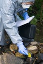 A specialist, in a protective suit, records data on a tablet, from marked crime scenes with numbers, on a pond Royalty Free Stock Photo