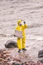 Specialist in protective suit checking sample of water on rocky sea shore