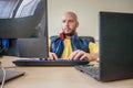The specialist is sitting in a chair in front of two displays. An office worker looks at the laptop screen. The man works at Royalty Free Stock Photo