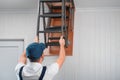 A specialist in uniform folds the attic ladder after installation