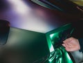 A specialist in wrapping a car with chameleon-colored vinyl film in the process of work.