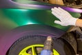 A specialist in wrapping a car with chameleon-colored vinyl film in the process of work.