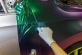 A specialist in wrapping a car with chameleon-colored vinyl film in the process of work.