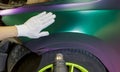 A specialist in wrapping a car with chameleon-colored vinyl film in the process of work.