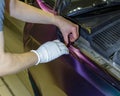 A specialist in wrapping a car with chameleon-colored vinyl film in the process of work.