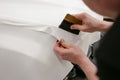 A specialist in wrapping a car with white vinyl film in the process of work.