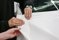 A specialist in wrapping a car with white vinyl film in the process of work.