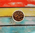 Specialty coffee concept. Roasted coffee beans in white cup on colorful striped wooden background top view