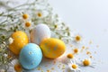Speckled vibrant colored eggs amidst a scattering of daisies and flowers on a blue surface, hinting at Easter's