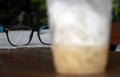 Spectacles on the newspaper and foreground out focus less cappuccino coffee in the plastic cup. Royalty Free Stock Photo