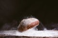 Spectacular image of fresh and rustic golden bread falling on wood kitchen table with flour explosion against black background. Royalty Free Stock Photo