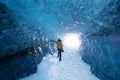 Spectacular natural landscapes inside a blue ice cave, with a woman in yellow looking outside the cave in Iceland