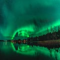 Spectacular night photo strong green lights of dancing Aurora over Northern forest, reflection in lake, small boat, bridge. Royalty Free Stock Photo