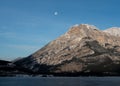 Spectacular scene of a full moon setting behind a mountain range in Lac Des Arcs, Alberta Canada.
