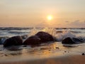 Spectacular view of a rocky beach at sunset with waves crashing on the rocks, colorful sky reflecting on the water, creating a Royalty Free Stock Photo