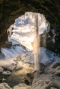 Spectacular waterfall in Iceland with guy looking at it at sunset time with water flowing through ceiling all snow covered Royalty Free Stock Photo