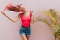 Spectacular woman in bright tank-top posing near palm tree. Indoor photo of winsome girl playing wi