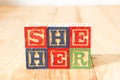 Spectacular wooden cubes with the word SHE HER on a wooden surface