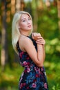 A spectacular young blonde woman with long hair elegantly poses outdoors against the background of trees in the summer.