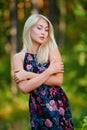 A spectacular young blonde woman with long hair elegantly poses outdoors against the background of trees in the summer.