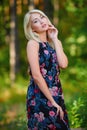 A spectacular young blonde woman with long hair elegantly poses outdoors against the background of trees in the summer.