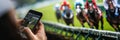 Spectator using a smartphone to bet on a horse race, blurred racetrack in the background Royalty Free Stock Photo