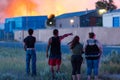 Spectators watch warehouse fire burning flames rage in the distance