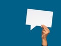 A speech bubble concept. Hand holding of an empty white speech bubble against a blue background Royalty Free Stock Photo