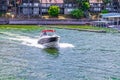 Speedboat speeds across a lake with condos and docks and a long pier on and near the shore on a summer day