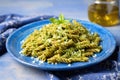 spelt pasta shape coated with pesto spotlighted on a blue plate