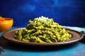 spelt pasta shape coated with pesto spotlighted on a blue plate