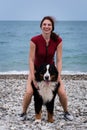 Spend time outside with dog and enjoy healthy life. Young pretty Caucasian red haired girl is sitting on Bernese mountain dog and Royalty Free Stock Photo