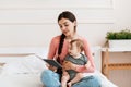 Spending time with baby. Young loving mom reading book to her infant daughter, relaxing together on bed at home Royalty Free Stock Photo