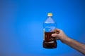 Spent cooking oil recycling in a clear plastic bottle. Held in hand by man. Close up studio shot, on blue background