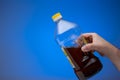 Spent cooking oil recycling in a clear plastic bottle. Held in hand by man. Close up studio shot, on blue background