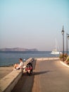 SPETSES, GREECE - 2019: Lady sitting watching the ocean with vespa