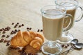 Spice latte or coffee with milk in the glasses decorated with fried coffee beans, croissants and vintage spoons on the brown cloth Royalty Free Stock Photo