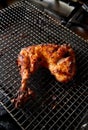 Spiced chicken leg on a wire rack grilled over charcoal.