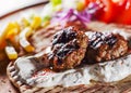 Spicy bifteki, frikadelle or frikkadel meatballs with minced beef and lamb with pita bread, tzatziki dip, vegetables salad and Fre