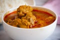 Spicy chicken gravy in a bowl. Chicken curry with rice in background