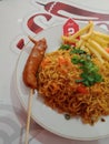 Spicy chili noodles are served with a round plate containing sausages and potatoes