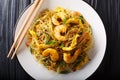 Spicy fried rice noodles with sausage, shrimps and vegetables close-up on a plate. Horizontal top view