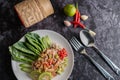 Spicy lime pork salad with kale, galangal, chilli and garlic in a white plate on a black cement floor Royalty Free Stock Photo