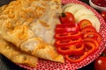 Spicy pie with cheburek meat with tomatoes, sweet pepper and ketchup lies in a flat plate on a dark wooden table. Delicious