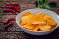 Spicy potato chips in white bowl and chili on wooden table Royalty Free Stock Photo