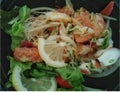 A spicy seafood salad consisting of salmon, squid, lemon, lemon, tomato and green leafy vegetables