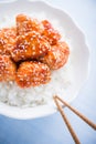 Spicy sweet and sour chicken with sesame and rice on blue wooden background