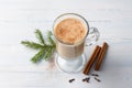 Spicy warming tea with milk in glass cup with cinnamon, gingerbread cookie tied with ribbon and Christmas tree branches