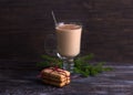 Spicy warming tea with milk in glass cup with cinnamon, gingerbread cookie tied with ribbon and Christmas tree branches