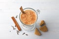 Spicy warming tea with milk in a glass cup and cinnamon sticks, cloves, with gingerbread cookie